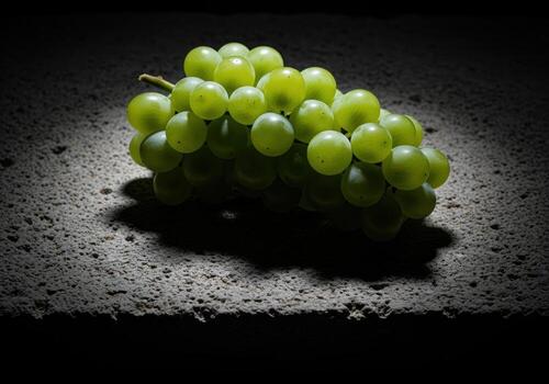 Vibrant green grapes illuminated dramatically on a textured dark stone surface. photo