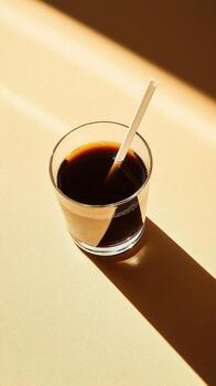 Morning Coffee in a Glass With a White Straw on a Light Surface and Sun Rays Creating Shadows photo