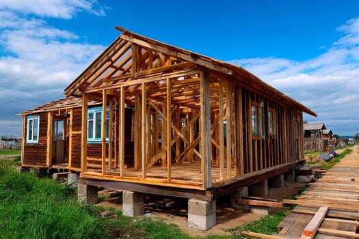 Newly built wooden houses are under construction in a rural setting. The framework is visible along with a neat pathway, showcasing ongoing development in the community photo