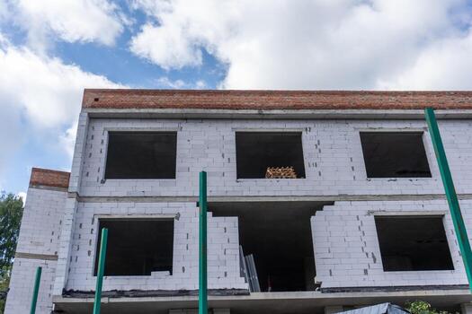 Construction of a modern building with open windows and green columns under a blue sky in a developing area photo