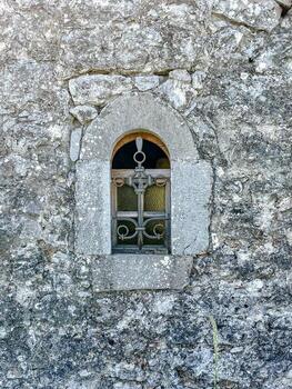 Rustic window set in a weathered stone wall. The rough texture of the rocks contrasts with the simple frame, creating a timeless architectural detail. High quality photo