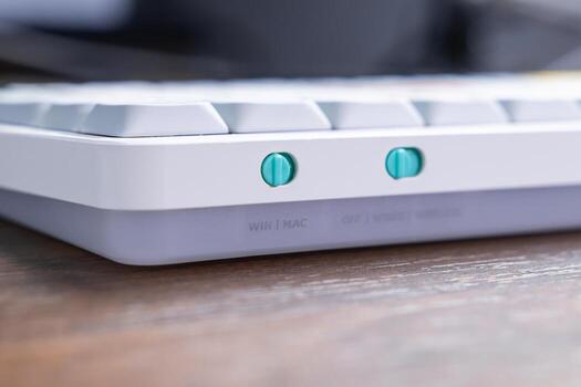 Close-up of a modern white mechanical keyboard featuring distinct teal toggle switches for WIN MAC operating system selection and versatile wired wireless connectivity options photo