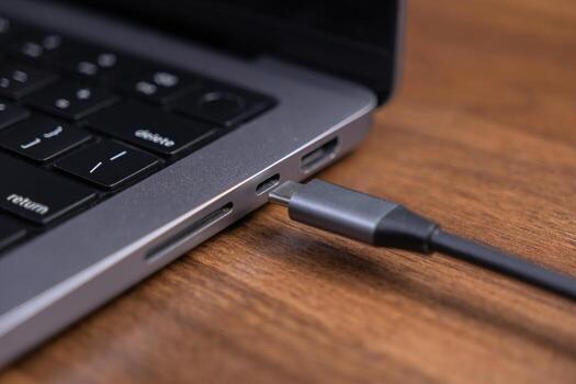 Modern gray laptop features a black USB-C cable securely plugged into its side port, emphasizing reliable, efficient power charging and fast data transfer for productive digital tasks photo