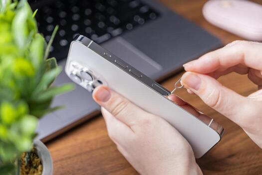 Hands precisely using a SIM ejector tool to access the card slot of a sleek, modern smartphone, demonstrating essential mobile network configuration photo