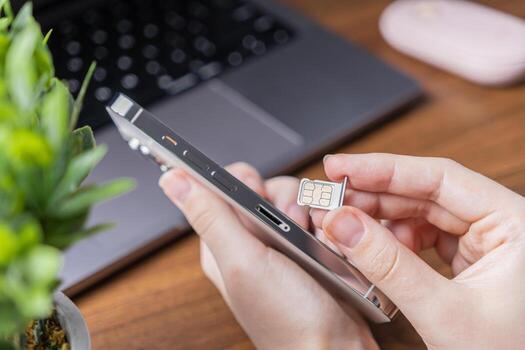 Human hands inserting a micro SIM card into a modern silver smartphone, symbolizing mobile network connectivity and essential telecommunication device setup on a busy desk photo