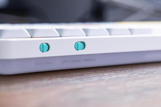 White mechanical keyboard featuring bright teal toggle switches for WIN MAC and OFF WIRED WIRELESS settings, facilitating adaptable user interface control photo