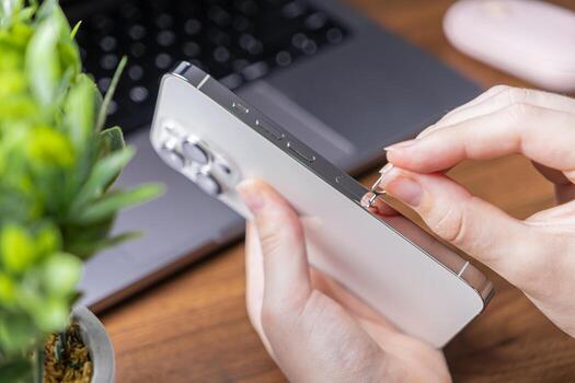 User's hands inserting a SIM ejector tool into a sleek smartphone, preparing to open the SIM card tray for mobile connectivity or device activation photo