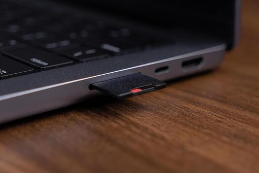 Black SD card partially inserted into a modern laptop's memory slot, representing digital data storage and efficient multimedia file transfer for technology photo
