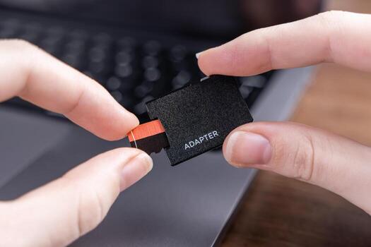 Human hands carefully connect a small microSD memory card into a black ADAPTER, enabling seamless digital data transfer and storage photo
