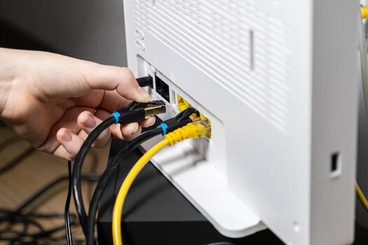 Human hand plugging a black Ethernet cable into a white internet router, establishing a secure network connection for modern digital technology setup photo