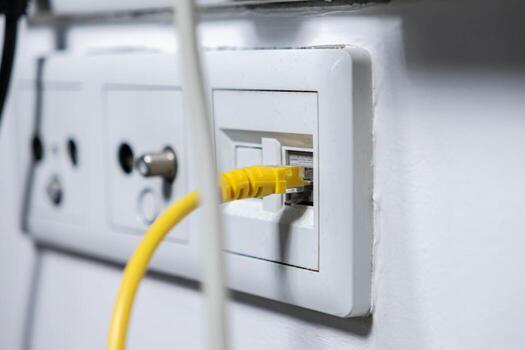 amarillo ethernet cable atascado dentro un blanco pared enchufe, simbolizando rápido Internet conexión, sin costura datos transferir, y de confianza hogar redes foto