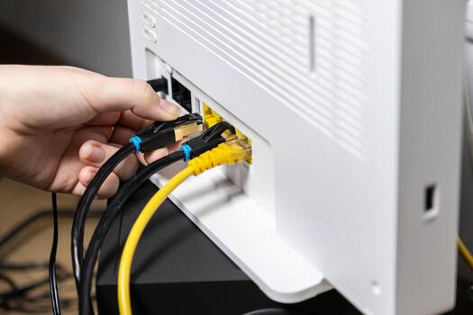 Adult hand firmly inserting a crucial black Ethernet LAN network cable into a modern white Wi-Fi router, enabling swift internet connectivity and robust digital network access photo