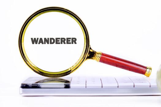 A magnifying glass, with the word Wanderer in its lens, is positioned over a computer keyboard on a white background. Focus is on discovery and exploration photo