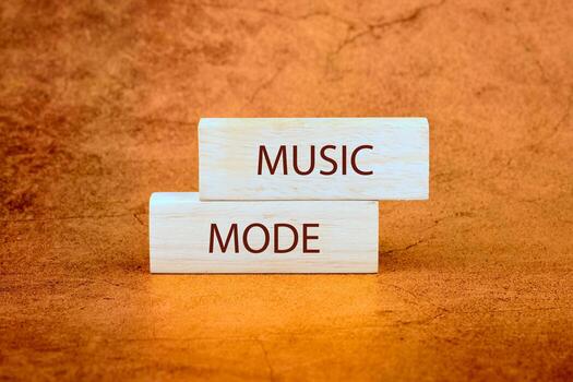 Two wooden blocks are stacked on a textured orange surface. The word MUSIC is printed on the top block, and MODE is printed on the bottom block photo