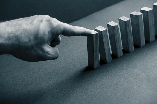 Domino has Fallen in a Row. Domino theory. Effect. Hand with Finger is Pointing and the Falling Wood Blocks. Risk Management, Revolution Concept. Affect Business. Closeup. Manifestation. Red photo