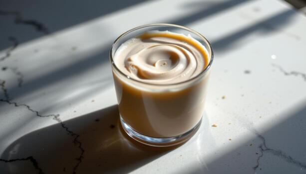 A mousse in a glass cup is illuminated from one side, revealing smooth transitions between light and shadow across its surface. photo
