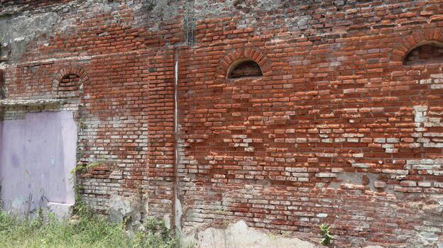 Old brick wall shows signs of decay with arched windows in a historic building, creating a sense of age and history. photo