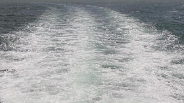 Boat's wake creates foamy path across the ocean surface, showcasing the movement and energy of the vessel, creating a dynamic and visually striking scene. photo