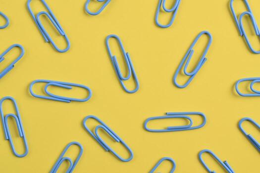 Overhead view of blue paper clips scattered across a vibrant yellow background, creating a playful pattern. photo