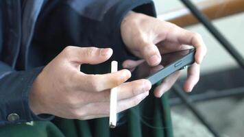 mani impegnato con un' mobile Telefono mentre Tenere un' illuminato sigaretta, cattura un' Comune contemporaneo scena di digitale interazione e un' fumo abitudine nel un' casuale ambientazione video