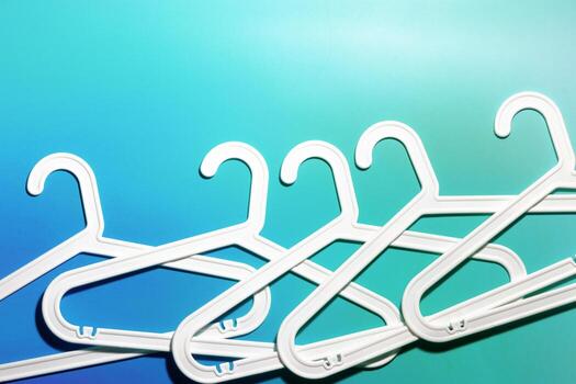 Row White Plastic hangers as minimal layout on soft gradient background of teal blue tones, Clothes rack for organizing clothes in closets or retail stores for hanging of garments, top view photo