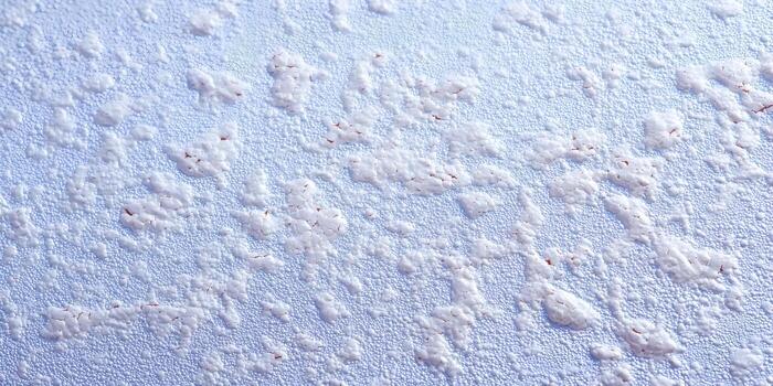 A textured surface displays white granular frost patterns and tiny particles on a light blue background with reddish hints photo