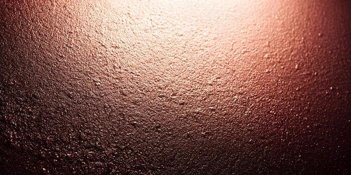 un texturizado rojizo marrón superficie con un áspero granular modelo es iluminado por un calentar diagonal ligero foto