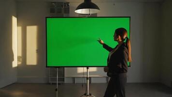 självsäker affärskvinna i en kostym presenter information på en grön skärm under en möte, använder sig av en pekare till markera nyckel poäng och engagerande med henne publik i en professionell miljö video