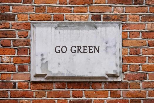 A GO GREEN message is displayed on a weathered stone tablet, set into a textured red brick wall, suggesting a commitment to eco-friendly practices photo