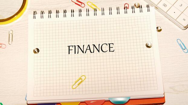 A spiral notebook with the word Finance written on the grid paper is seen on a desk with a calculator and colorful paper clips, representing financial planning photo