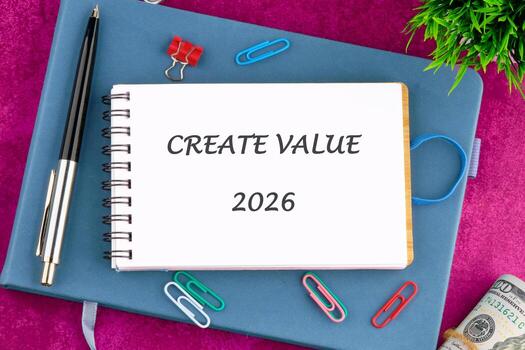 A notebook displaying the words CREATE VALUE 2026 sits on a blue notepad, alongside paperclips, a pen, and a rolled-up hundred dollar bill, signifying financial growth and planning photo