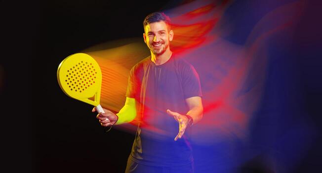 Man smiling and holding a yellow paddle racket in a colorful light setting photo