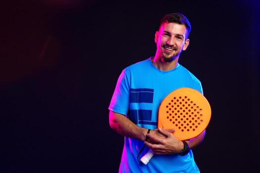 Man smiling while holding a bright orange paddle in a colorful studio setting photo