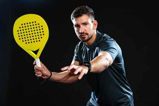 Man preparing to hit a ball with a yellow paddle in a dark studio setting photo