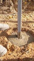 installer pressing post into wet concrete for fence footing, boots and jeans standing close as concrete rings form, smoothing edges and ensuring vertical alignment, curing in shaded backyard video