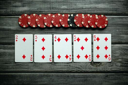 Five red diamond cards are laid out sequentially on a rustic wooden table, accompanied by a stack of red and black poker chips, suggesting an exciting card game in progress photo