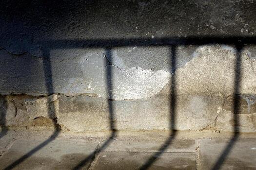 The shadow from the fence at the junction of the tiled sidewalk to the wall of the house foundation photo
