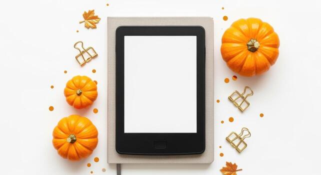 Ereader atop a notebook with pumpkins and fall leaves creates a seasonal flat lay scene photo