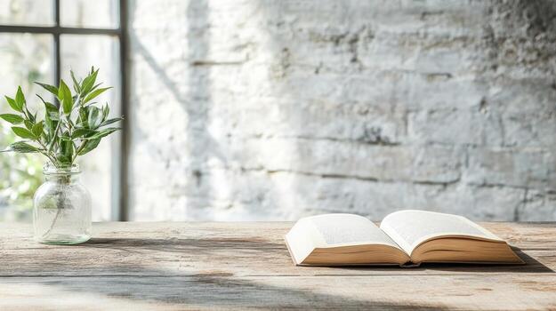 An open book and a vase of green leaves on a wooden table photo