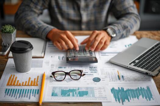 Business professional analyzing financial data with calculator, coffee cup, and documents on wooden desk, showcasing analytical skills and workspace organization photo