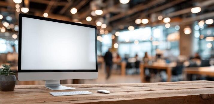 Modern desktop computer with blank screen on wooden table in contemporary workspace, featuring blurred background of busy office environment with warm lighting and inviting atmosphere photo