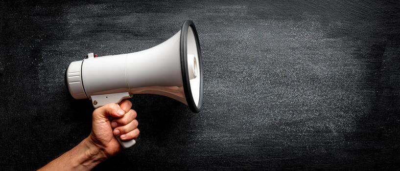 Hand holding a white megaphone against a dark textured background, symbolizing communication, announcement, and the power of voice in conveying messages effectively photo