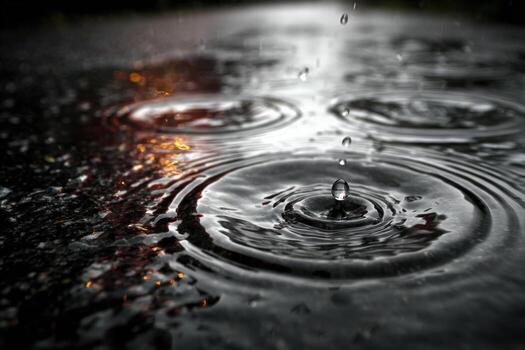 Close-up view of raindrops creating ripples on a dark surface, with reflections of light in the water, capturing the essence of a rainy atmosphere and nature's beauty photo