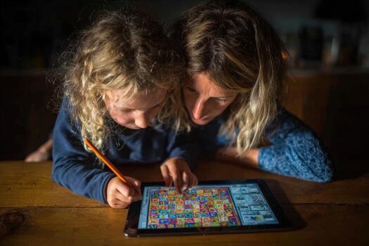 Mother and child engaged in interactive game on tablet, sharing joyful moments together, surrounded by warm ambient lighting in a cozy home environment photo