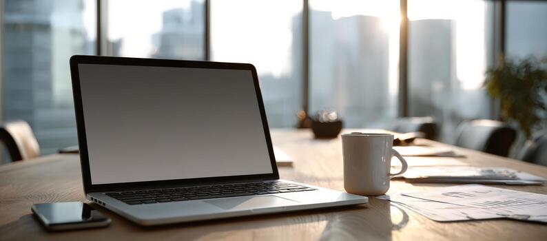 Laptop mock up with blank screen on wooden table, accompanied by a coffee cup and smartphone, in a modern office environment with large windows and city view photo