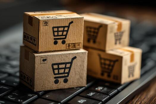Small cardboard boxes with shopping cart icons are stacked on a keyboard, symbolizing online shopping, e-commerce, and the convenience of digital retail experiences photo
