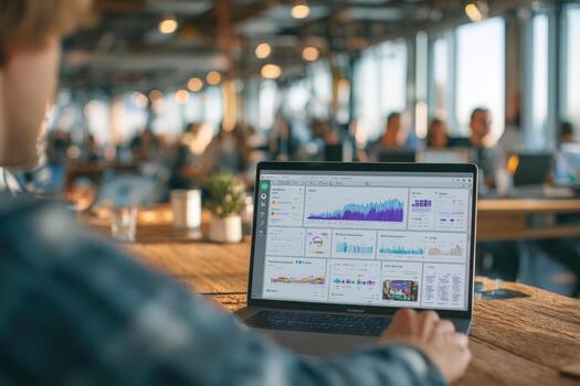 Individual working on laptop displaying data analytics in a modern office environment, with collaborative workspace and people engaged in discussions around, showcasing productivity and teamwork photo
