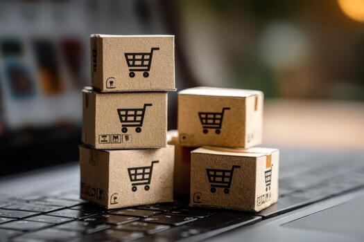 Stacked cardboard boxes with shopping cart icons are placed on a laptop keyboard, symbolizing online shopping and e-commerce, showcasing modern retail concepts and consumerism photo