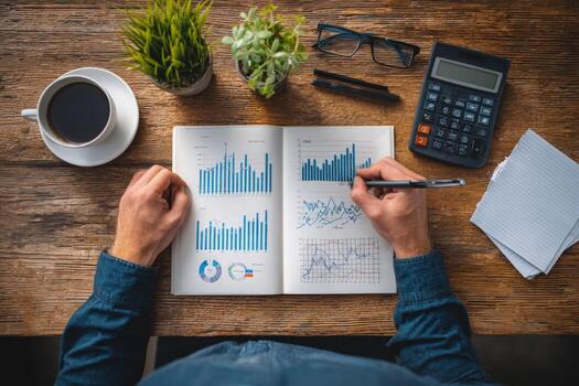 Individual analyzing financial data in a notebook, surrounded by coffee, calculator, and stationery, showcasing a productive workspace with graphs and charts photo