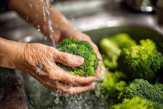 Hands of a person washing fresh broccoli under running water in a kitchen sink, showcasing the importance of cleanliness and preparation in healthy cooking practices photo